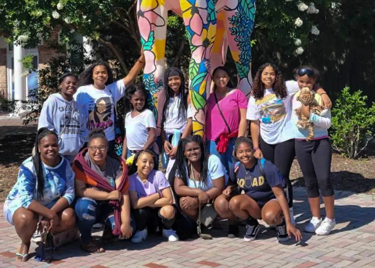 A group of 12 teenage girls pose for a photo in front of a giraffe statue during a trip to Viriginia.