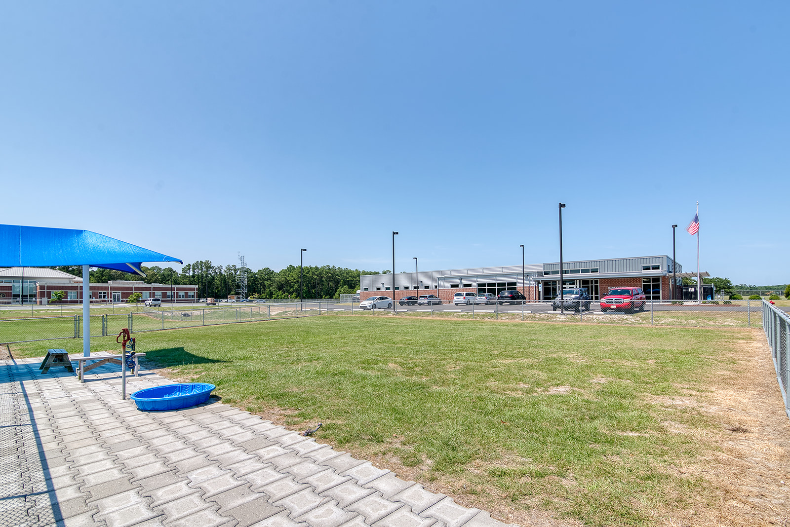 Image of the large fenced green space at the Manteo dog park. The animal shelter sits in the distance.