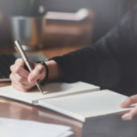 Image of a woman taking notes in a notebook using a pen.