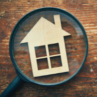 Image of a small wooden house figurine under a magnifying glass.