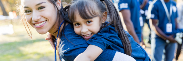 Image of a smiling little girl jumping onto a woman's back.