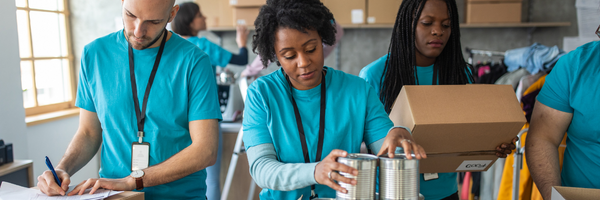 Image of three volunteers packing boxes of canned food at a food pantry.