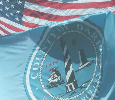 Image of an American flag and Dare County flag flying on a sunny day.