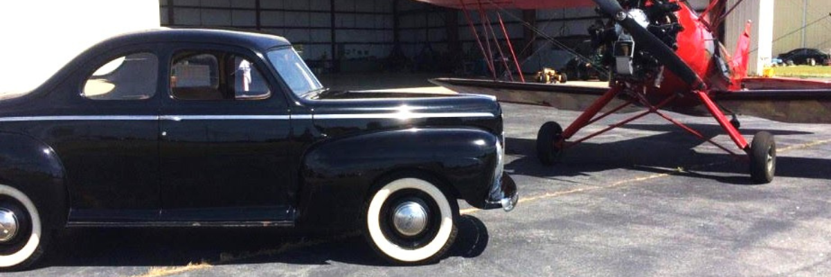 Image of an antique black car parked beside a small red plane.