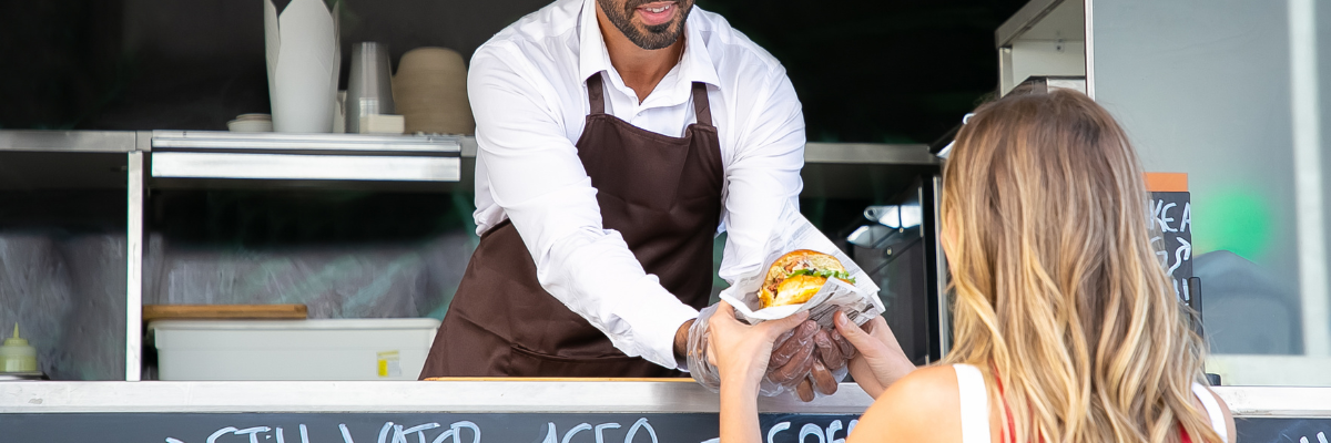 Image of a man handing a woman a burger out of a food truck.