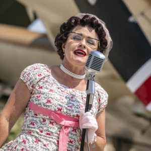 Image of Theresa Eaman singing in front an a vintage airplane.