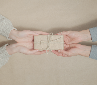 Image of one person giving another a gift wrapped in brown paper and twine.