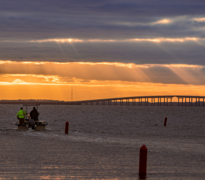 Image of a boat with two men cruising into a sunset on the water.