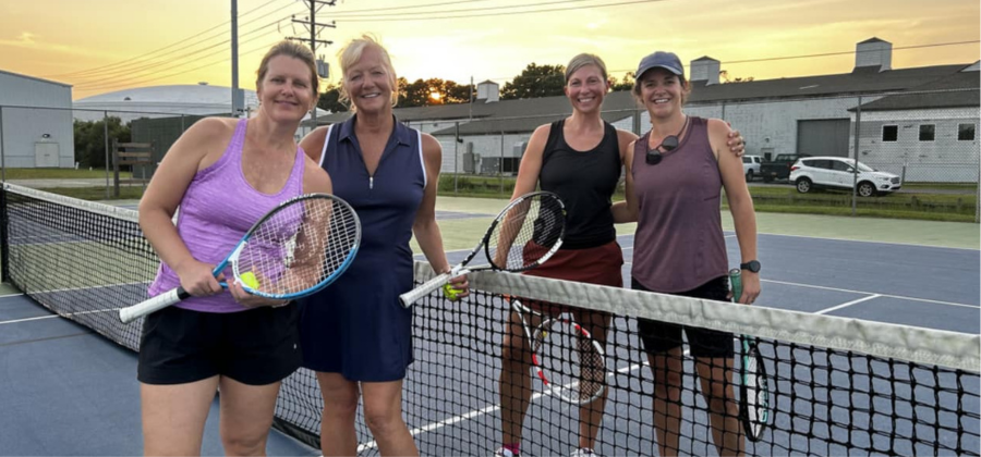 Four OBXTA women's league players stand together on a tennis court with the sun setting behind them.