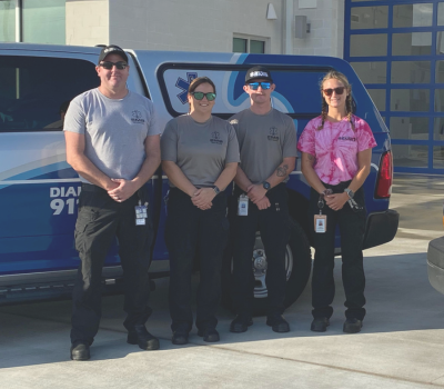 Image of four EMS employees standing in front of a medic unit.